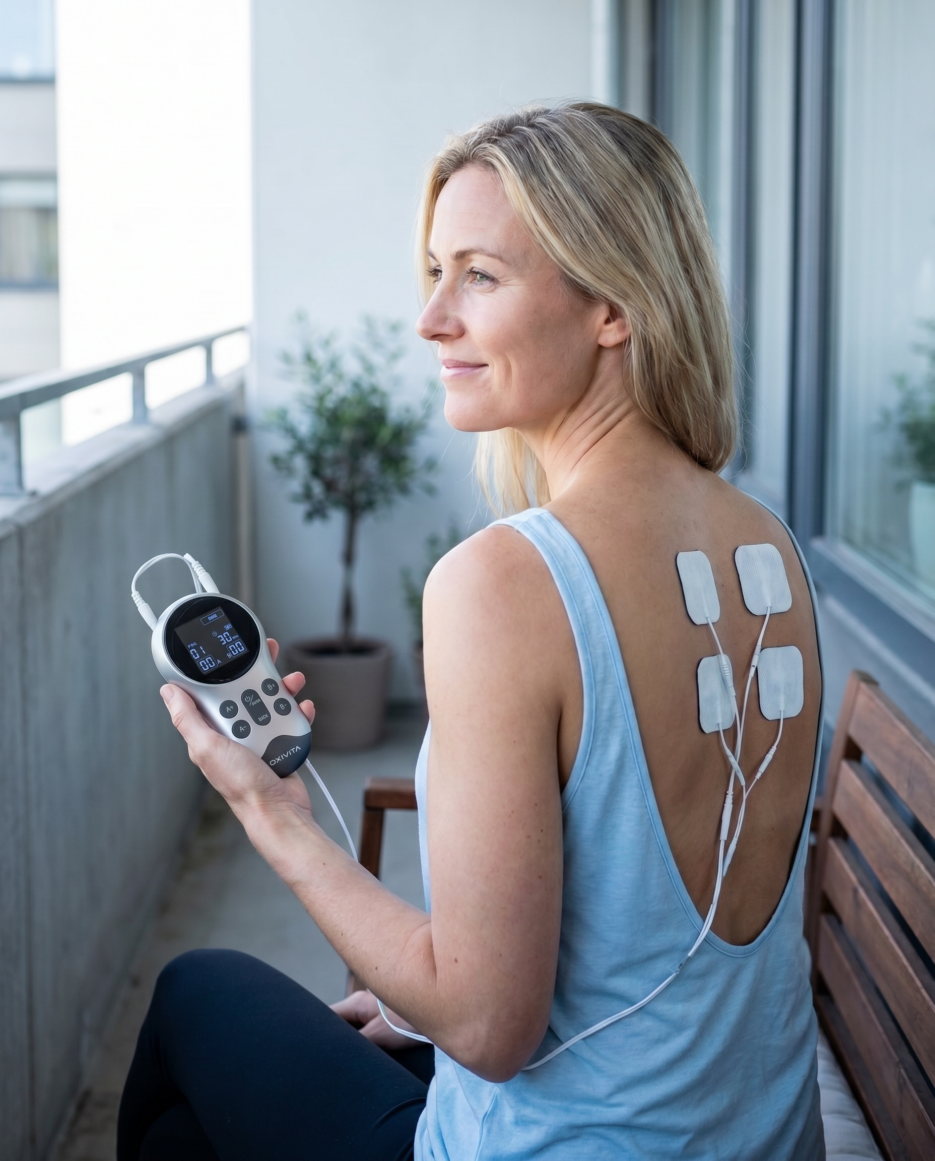 Kvinne bruker Oxivita Pulse T1 TENS-apparat med elektroder på ryggen mot ryggsmerter på balkongen
